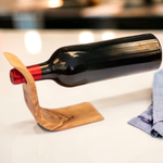 Olive wood balancing wine bottle holder with a wine bottle suspended at an angle